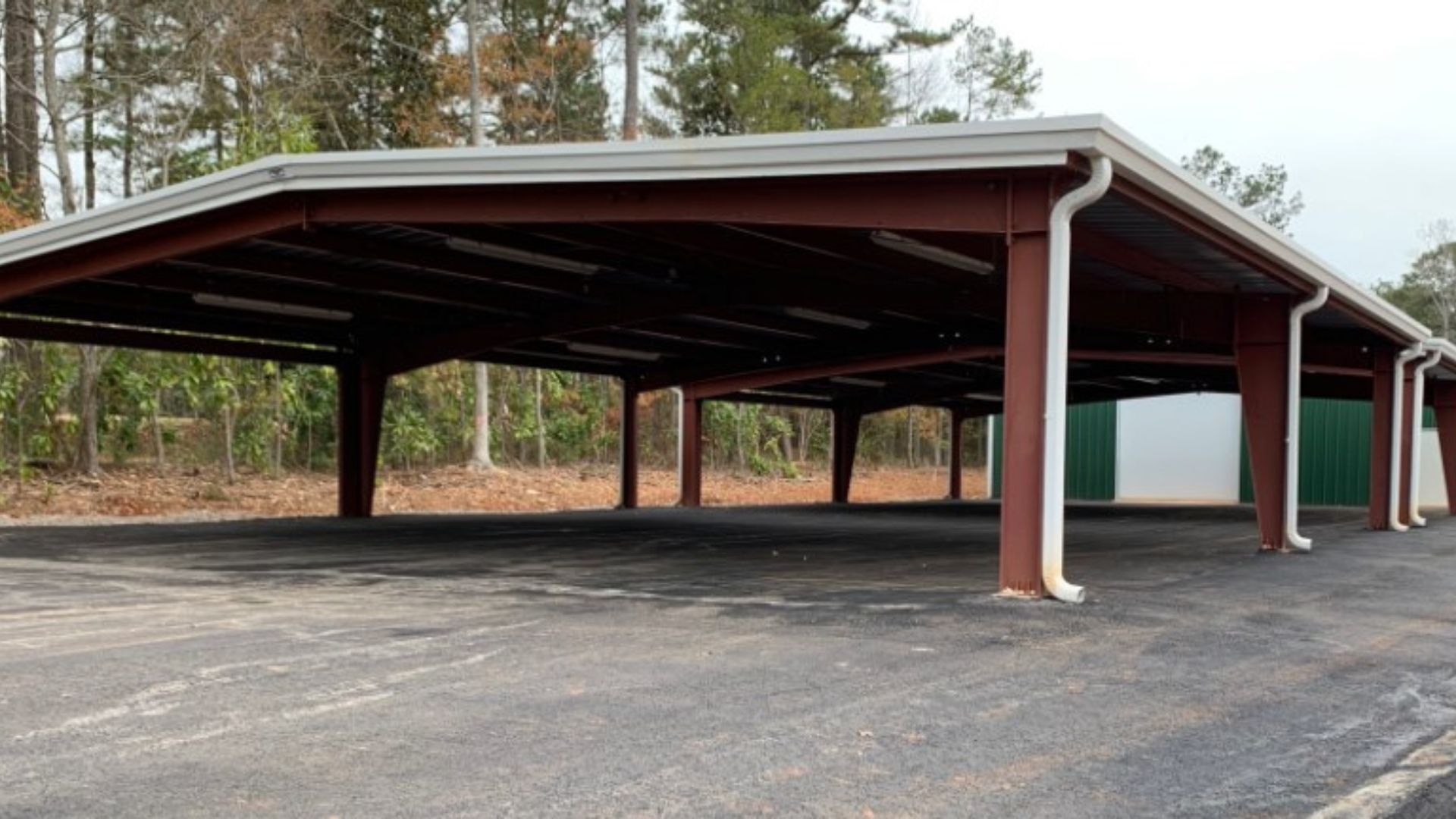 A row of parking spaces with a roof and gutters in a parking lot.