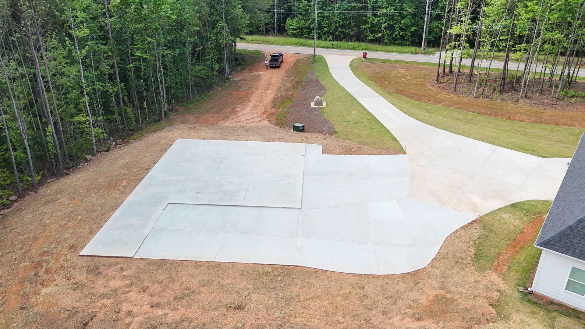 An aerial view of a concrete driveway surrounded by trees and dirt.