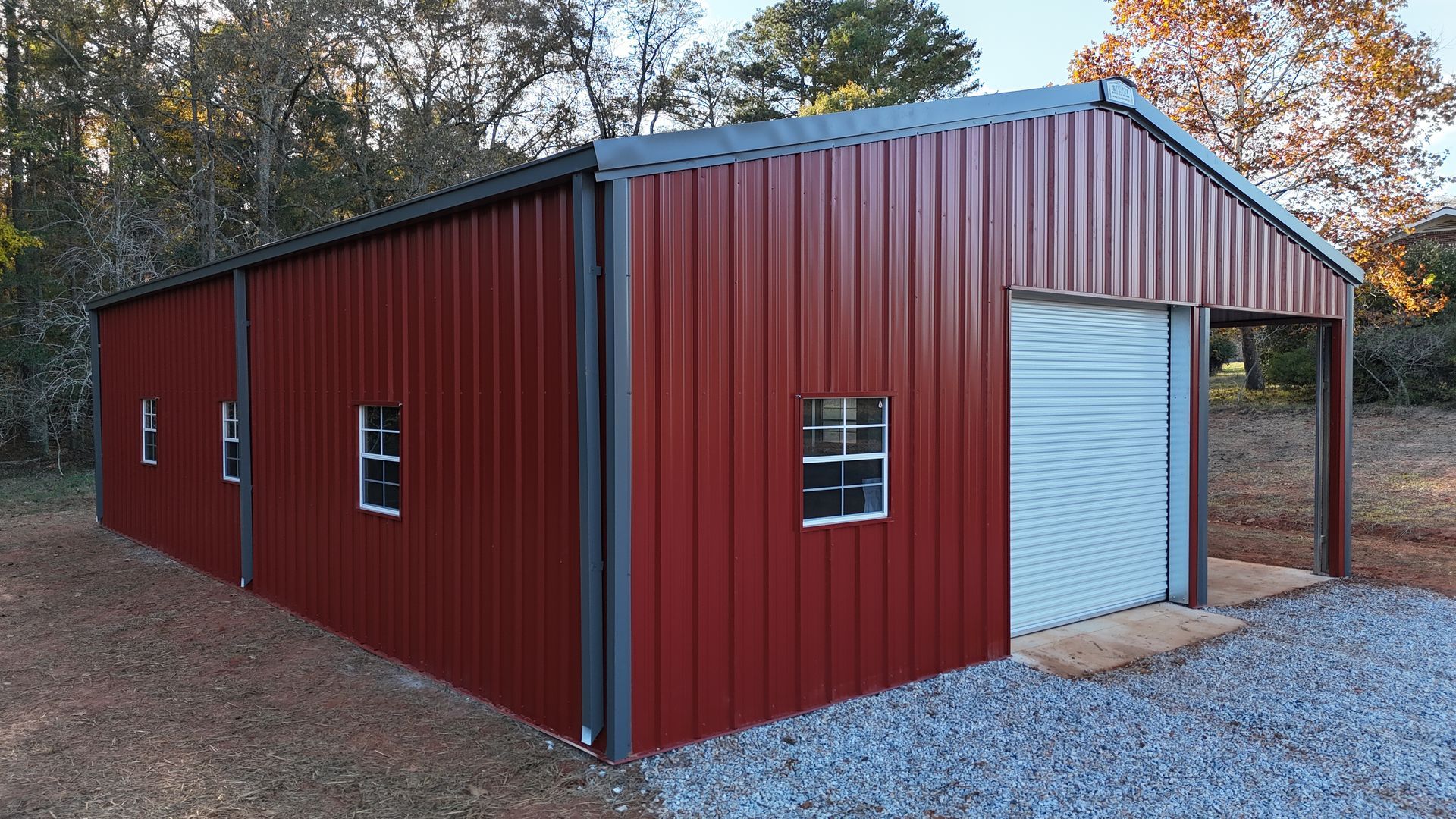 Red metal barn with gray trim and a roll-up door, set on gravel.