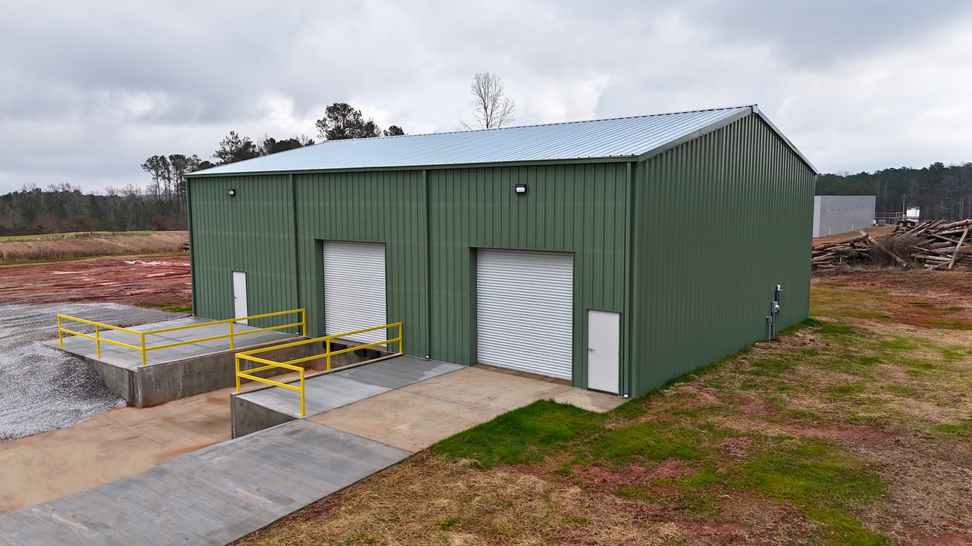 Green metal warehouse with loading docks, two roll-up doors, and a concrete ramp.
