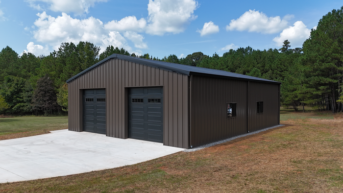 Brown metal garage building with two roll-up doors and a gravel driveway under a blue sky