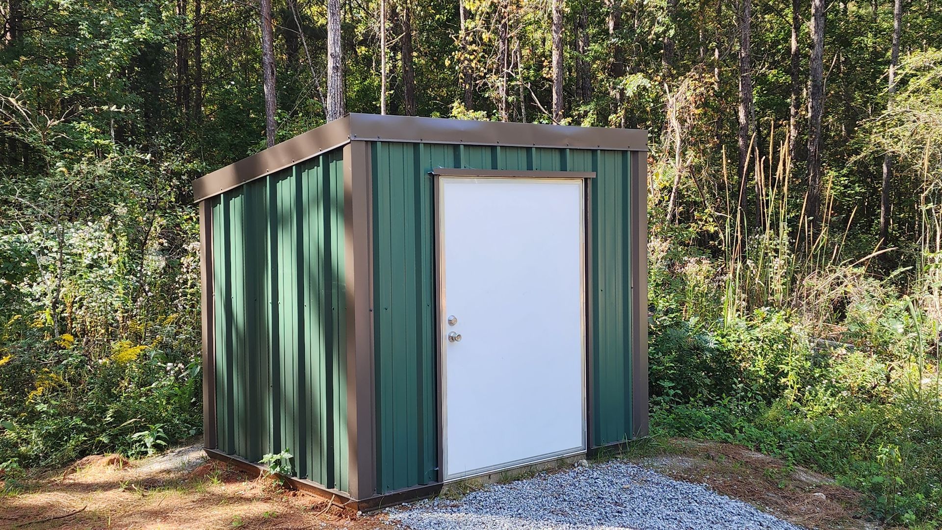 A green metal shed with a white door in the middle of a forest.