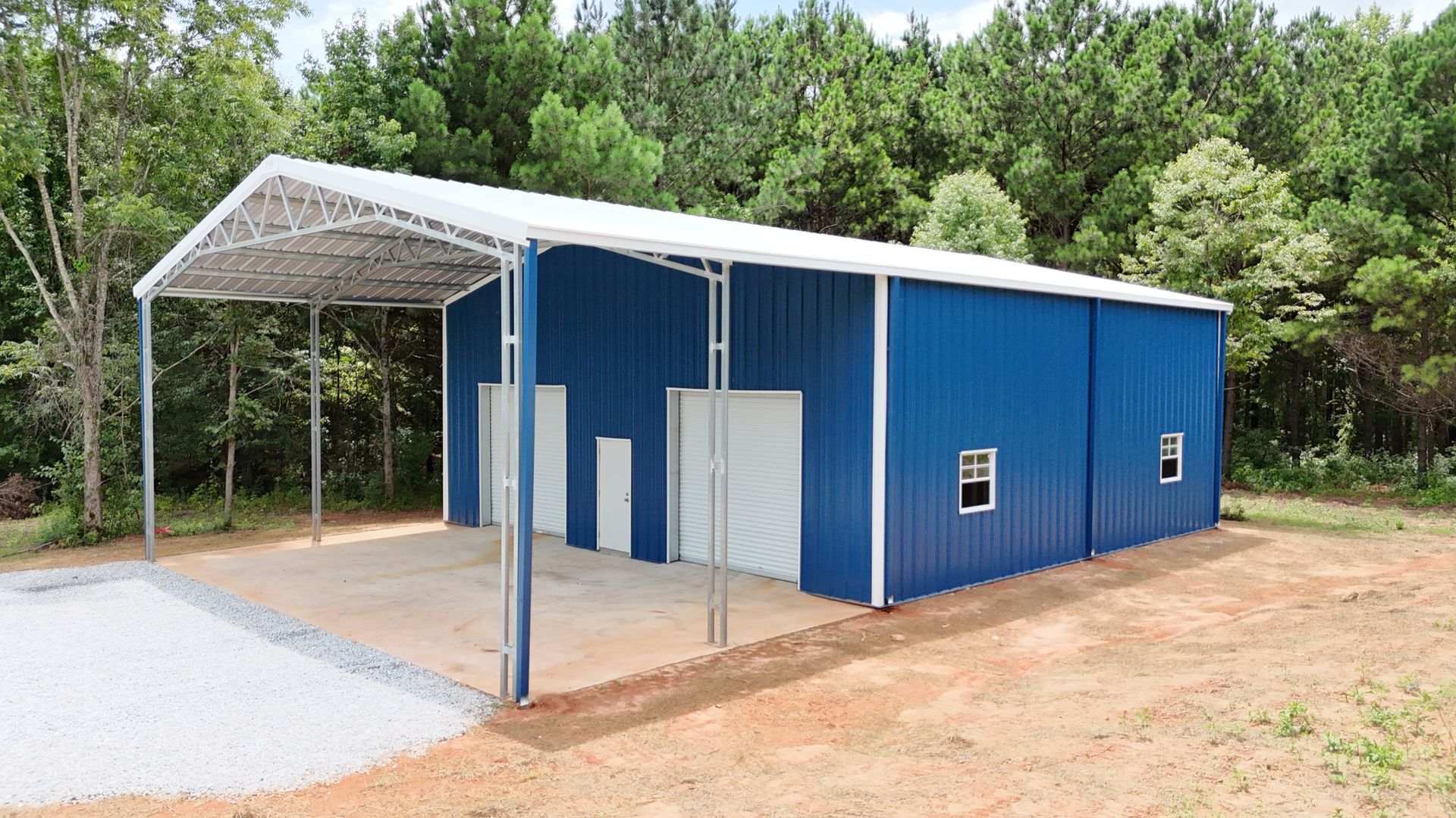 A blue metal building with a white roof is sitting in the middle of a dirt field.