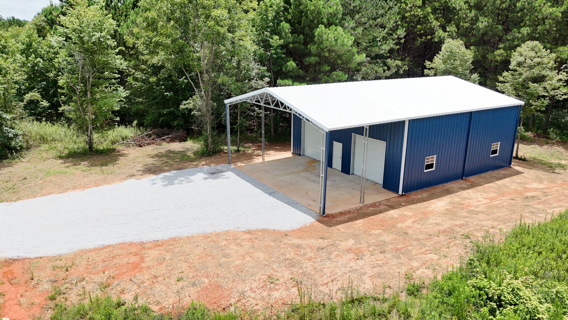 An aerial view of a blue building with a white roof in the middle of a field.