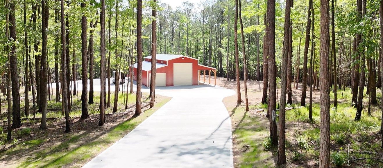 A driveway leading to a red garage in the middle of a forest.