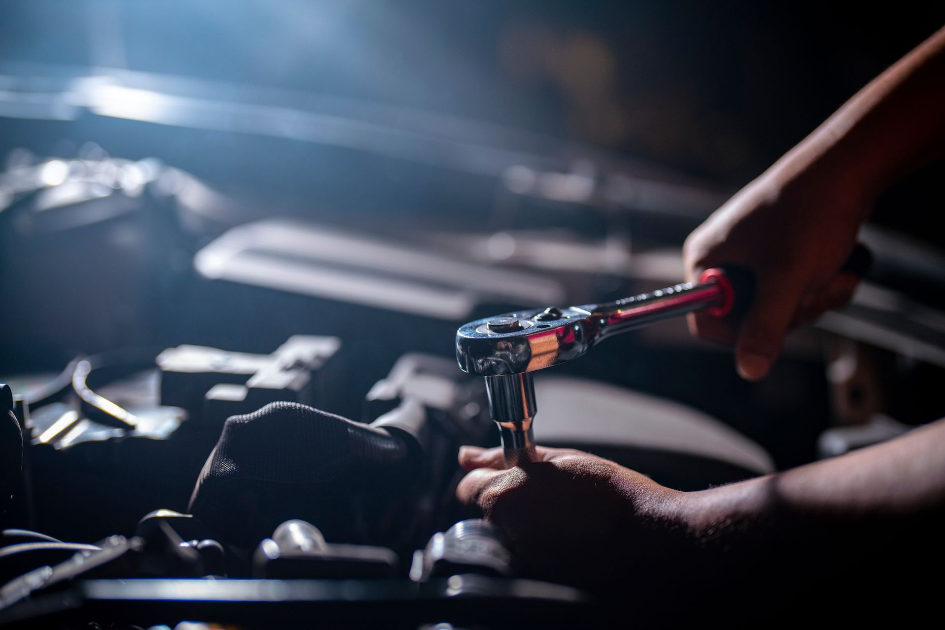 Hands using a wrench to work on a car engine under dim lighting.