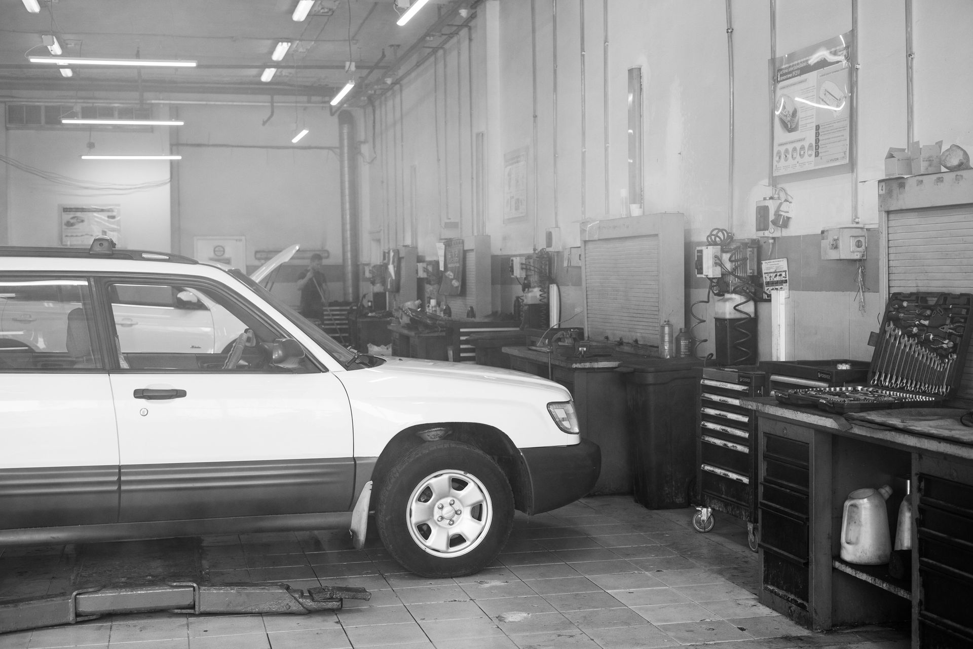White car in an auto repair garage beside workbenches and tools.