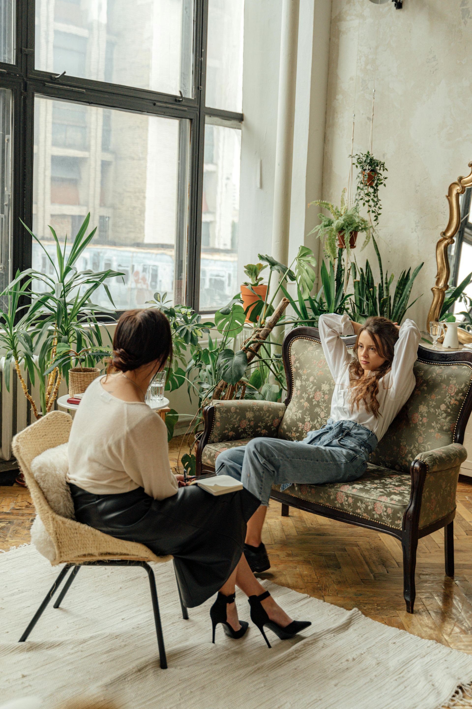 Two people talking in a bright plant-filled room, one seated across from the other in an armchair at Ripple and Root Therapy in Colorado