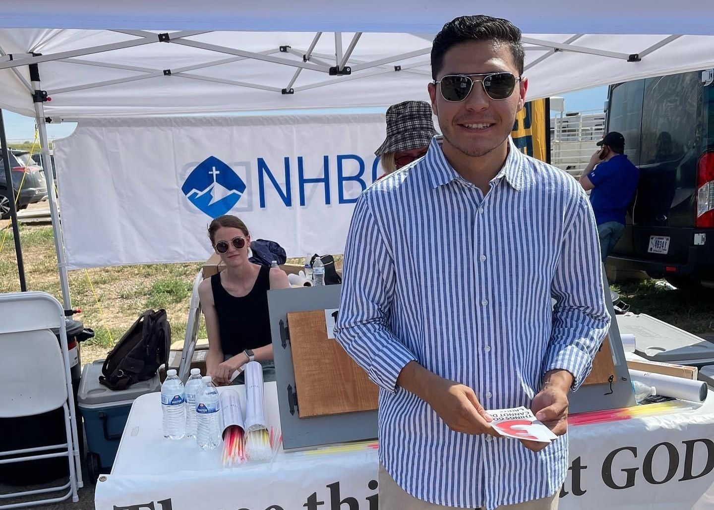 A man wearing sunglasses is standing in front of a nhb tent.