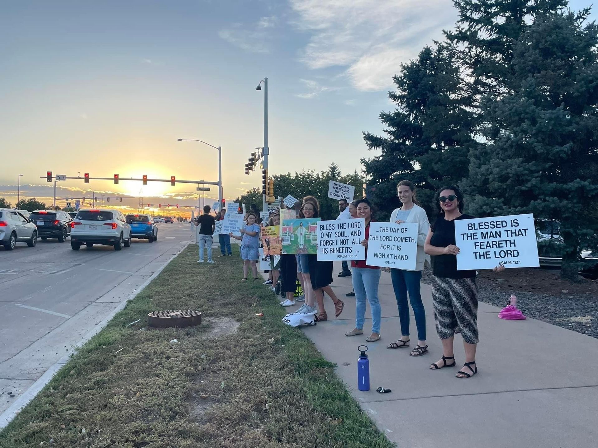 A group of people are standing on the side of a road holding signs.