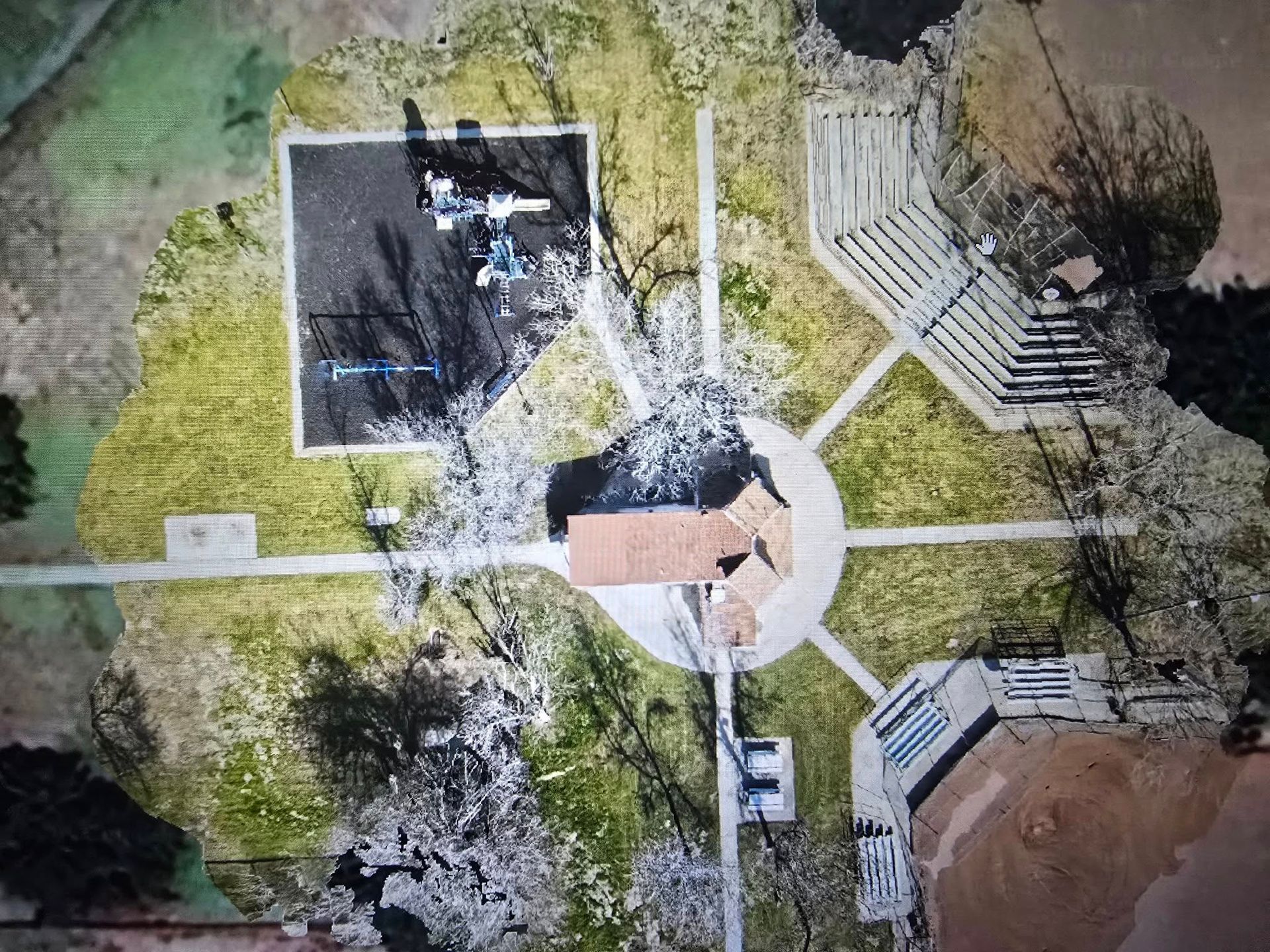 Aerial view of a circular park plaza with paths, benches, trees, and a small central building