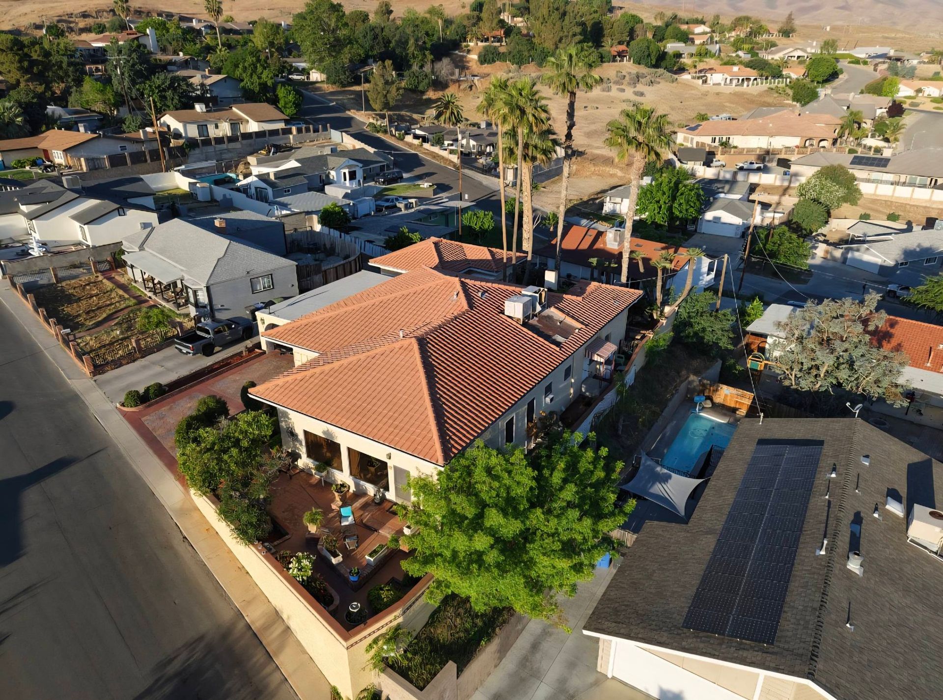 Aerial view of a suburban neighborhood with a red-roofed house and palm trees on a sunny day