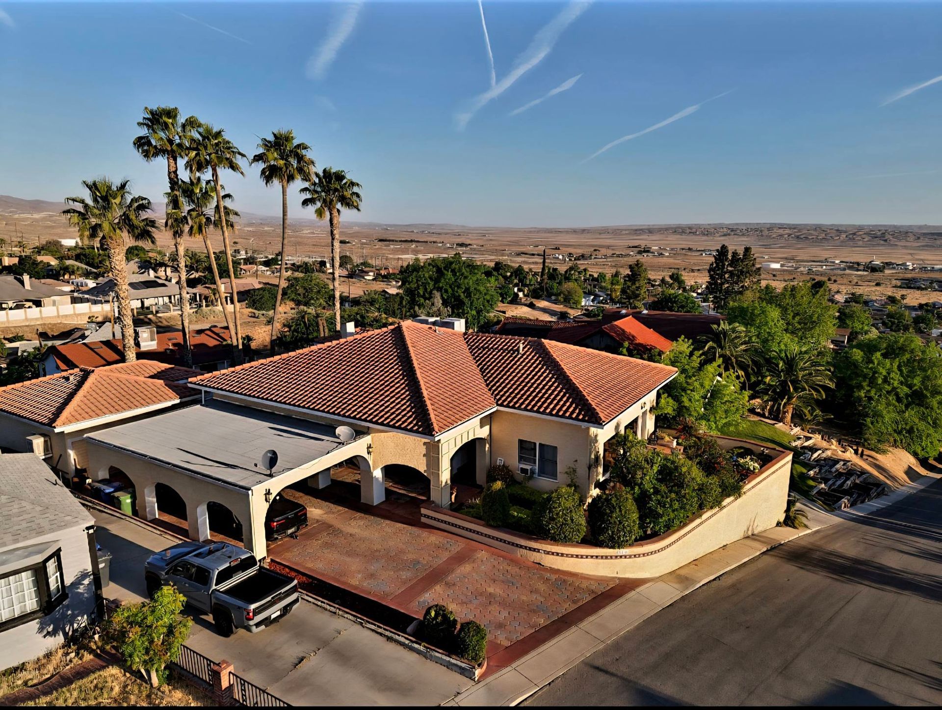 Aerial view of a suburban house with red tile roofs, palm trees, and a desert landscape under a clear sky