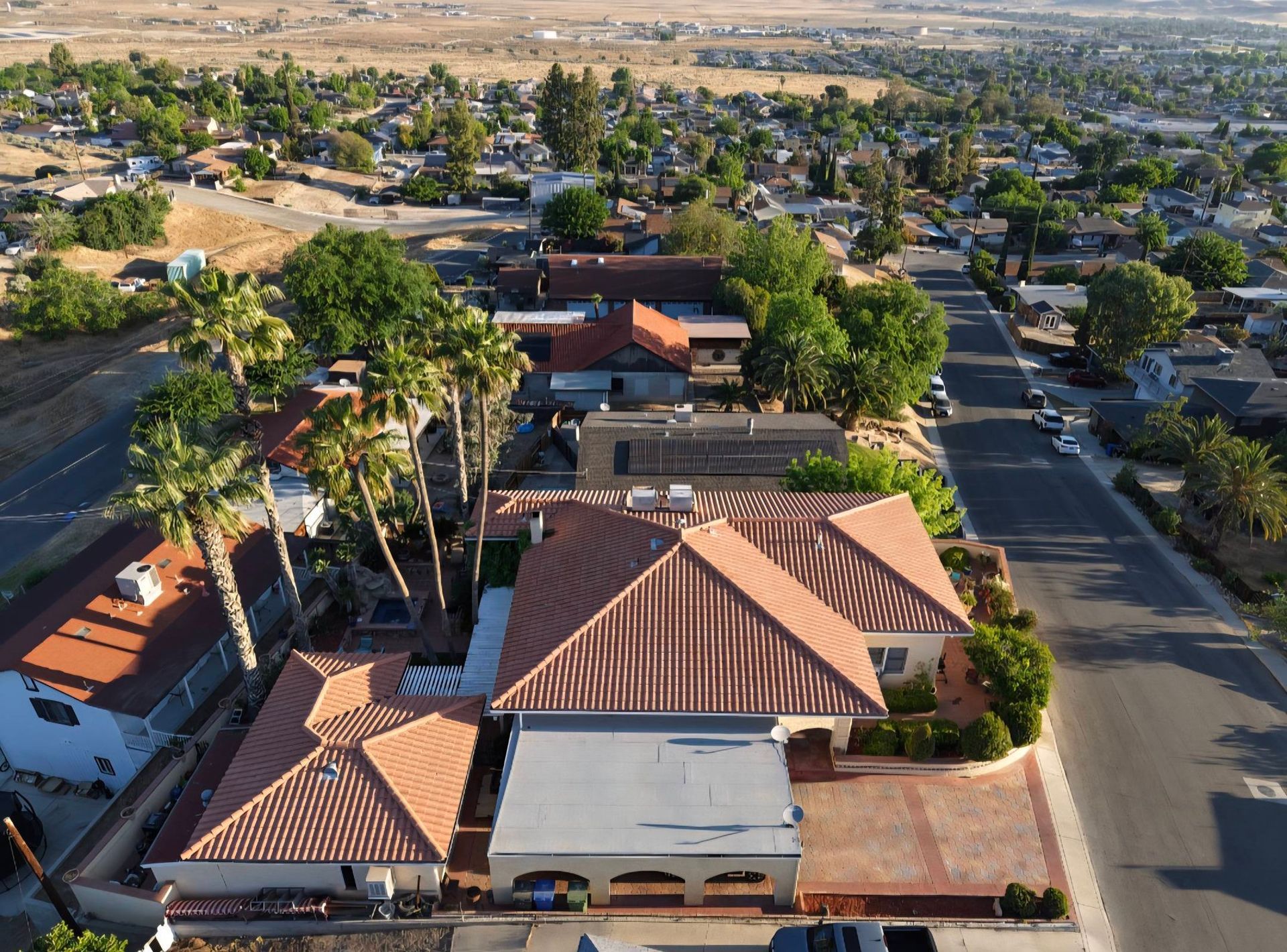 Aerial view of a suburban neighborhood with red-roofed houses, trees, and streets near open fields.