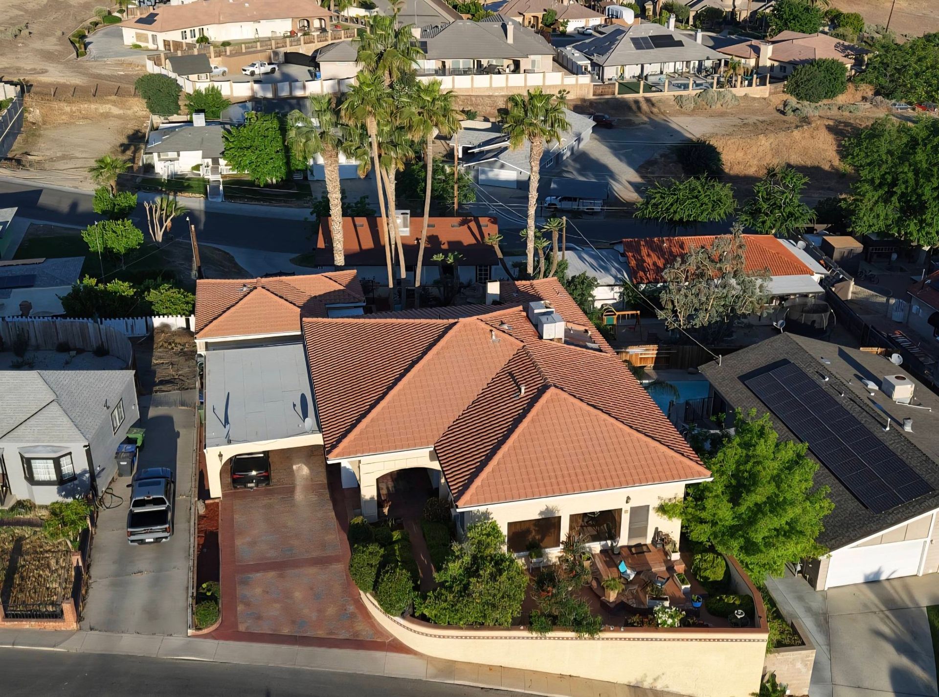 Aerial view of a tan-roofed suburban house with palm trees and a driveway in a residential neighborhood