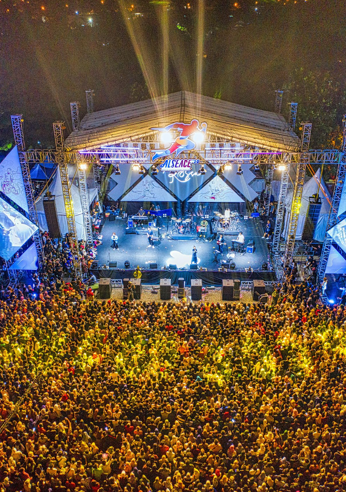 Outdoor concert stage at night with bright lights and a huge crowd of fans