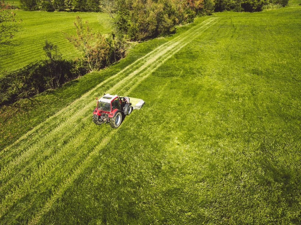 Red tractor mowing a bright green hillside field