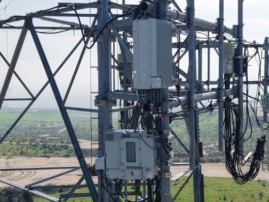 Steel telecom tower with mounted equipment and cables against a rural landscape