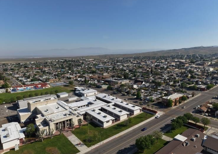 Aerial view of a suburban neighborhood with a white school campus beside a road under a clear blue sky