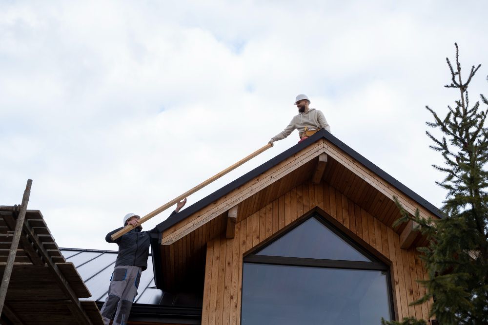 Two workers installing roofing on a wooden house under construction