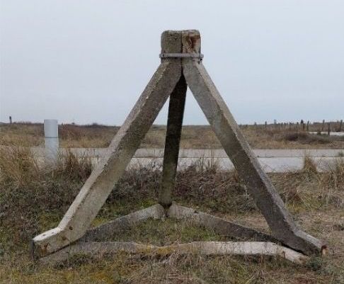 Driehoekige betonnen constructie op een grasveld, met een bewolkte hemel op de achtergrond.