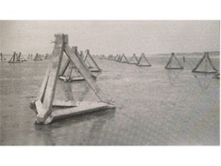 Driehoekige betonnen obstakels in ondiep water, waarschijnlijk een kustverdedigingswerk uit oorlogstijd.