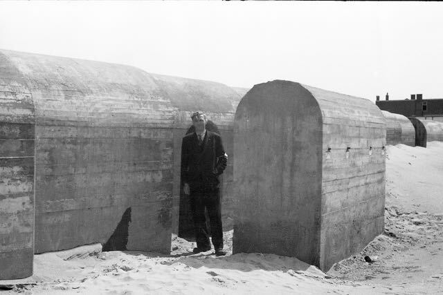 Een man staat in een betonnen constructie op een zandstrand.