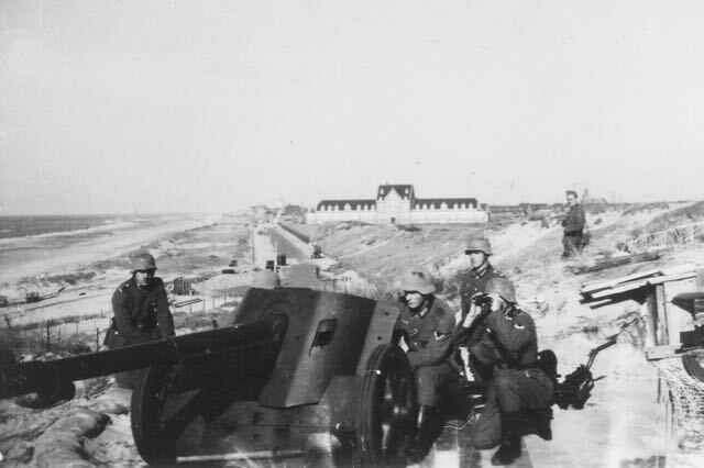 Duitse soldaten bemannen een antitankkanon in een kustbunker en richten het op een gebouw, tijdens de oorlog.