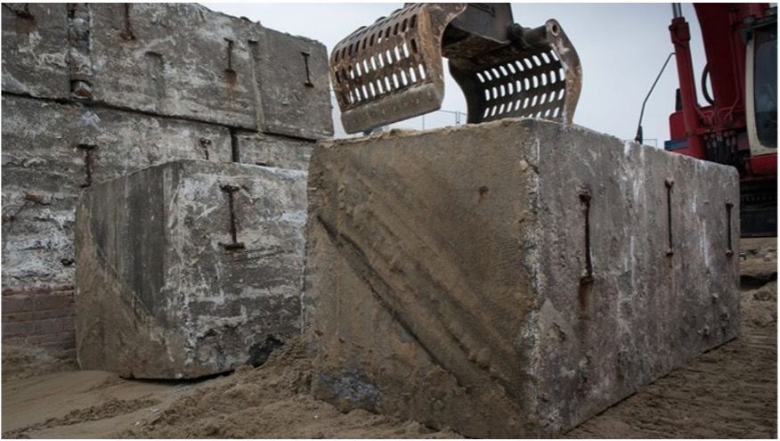 Betonblokken met metalen ankers worden verplaatst door een graafmachine.