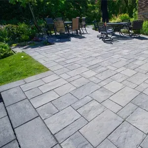 Stone patio with outdoor chairs and table beside a green lawn and trees