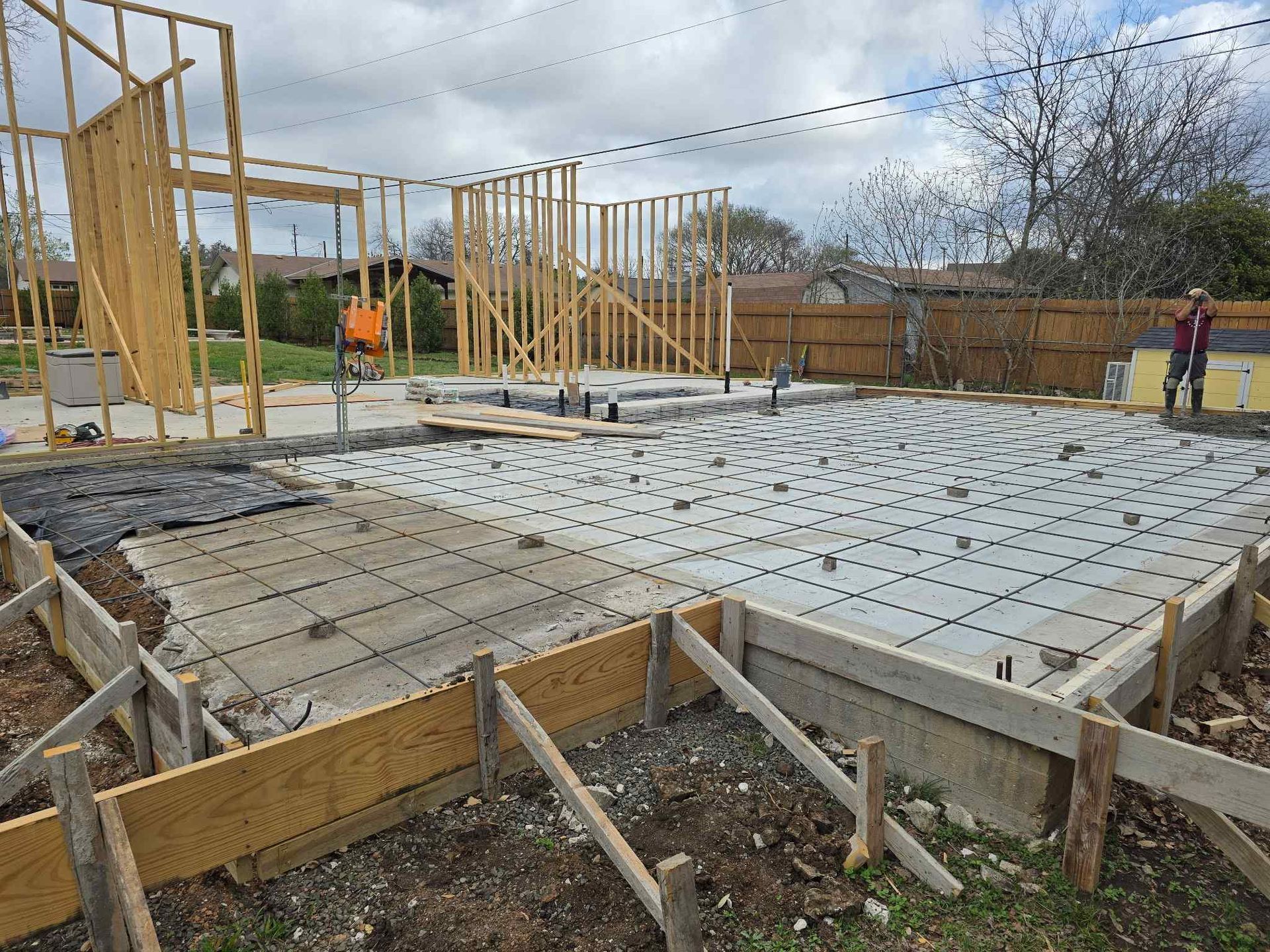 Construction site with concrete slab foundation, wooden framing, and workers in orange safety gear