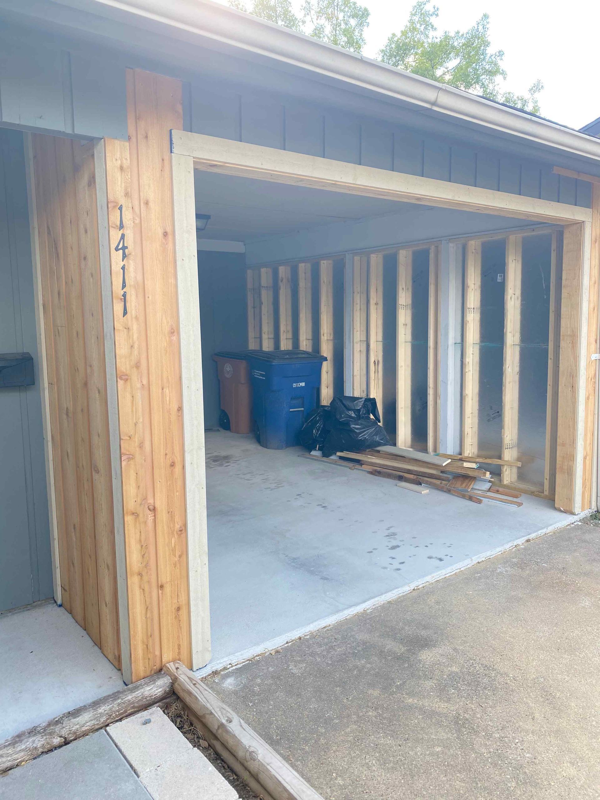 Open garage under construction with exposed studs, blue bins, and concrete floor