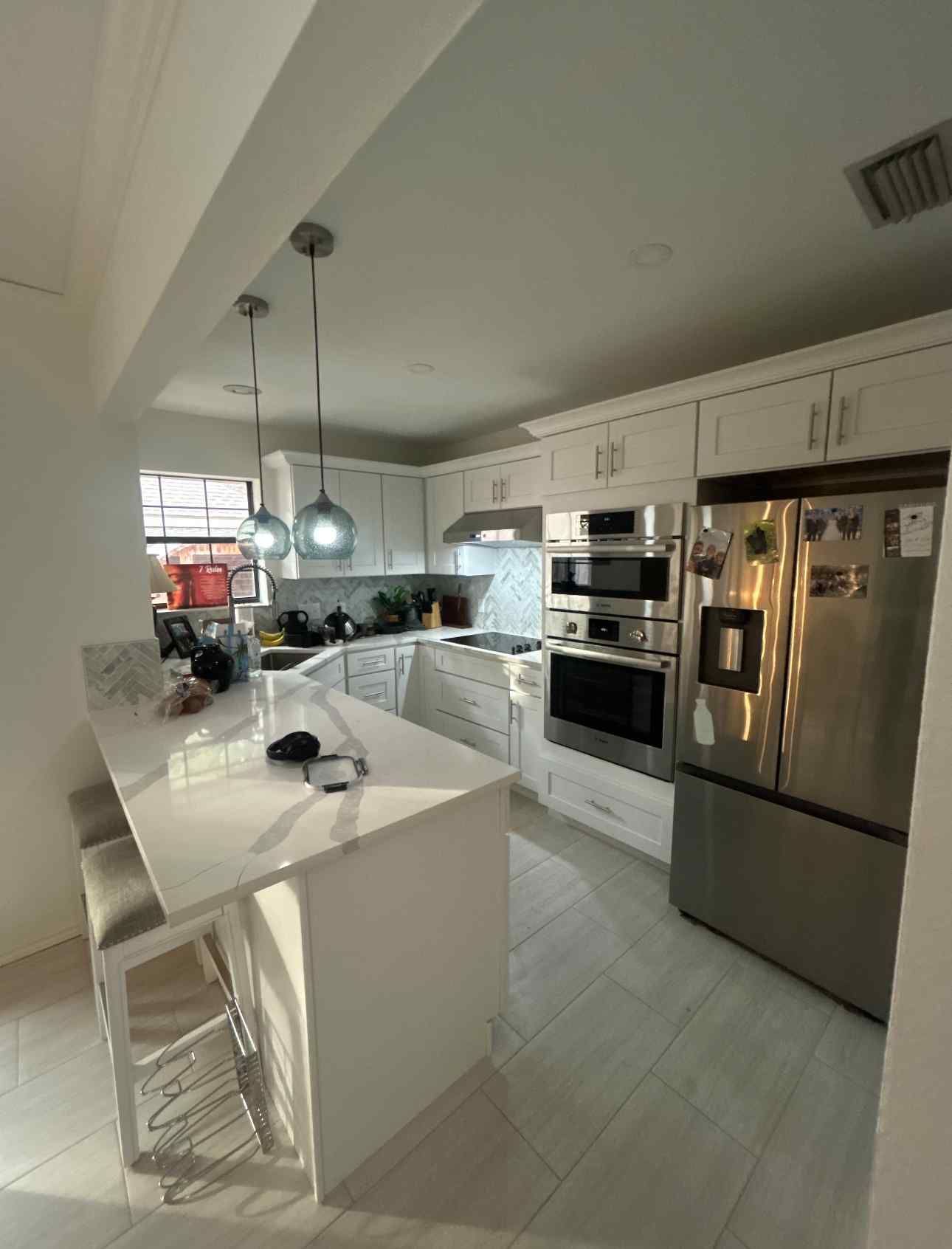 Bright white kitchen with island, stainless steel appliances, and pendant lights near a window.