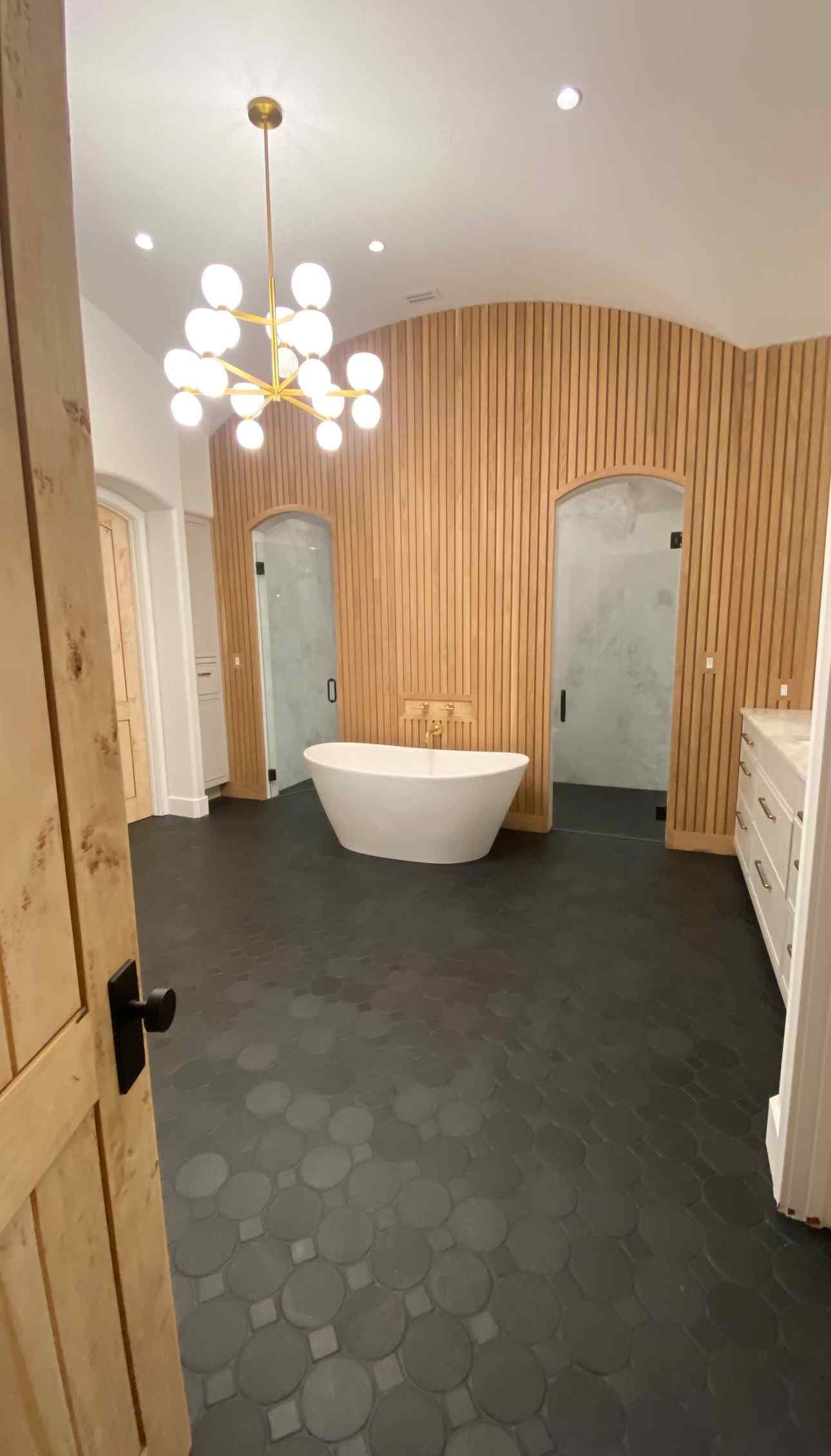 Modern bathroom with black hex tile floor, white tub, wood slat wall, and hanging pendant lights