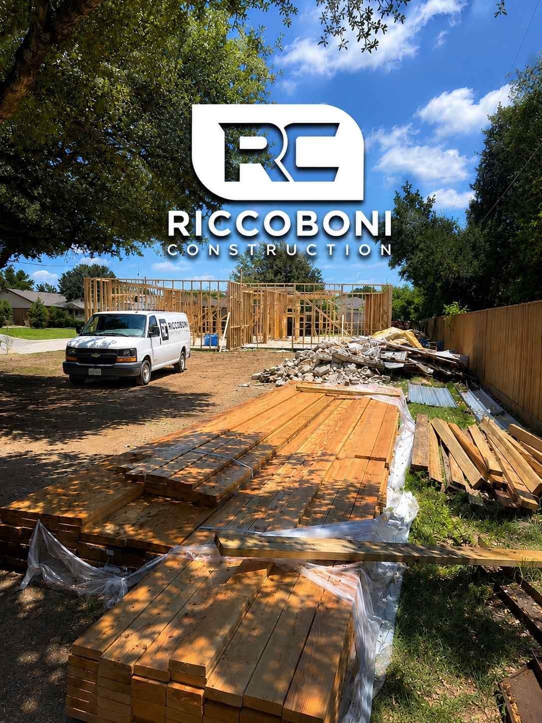 Construction site with building framework, lumber stacks, and a white truck under a blue sky.