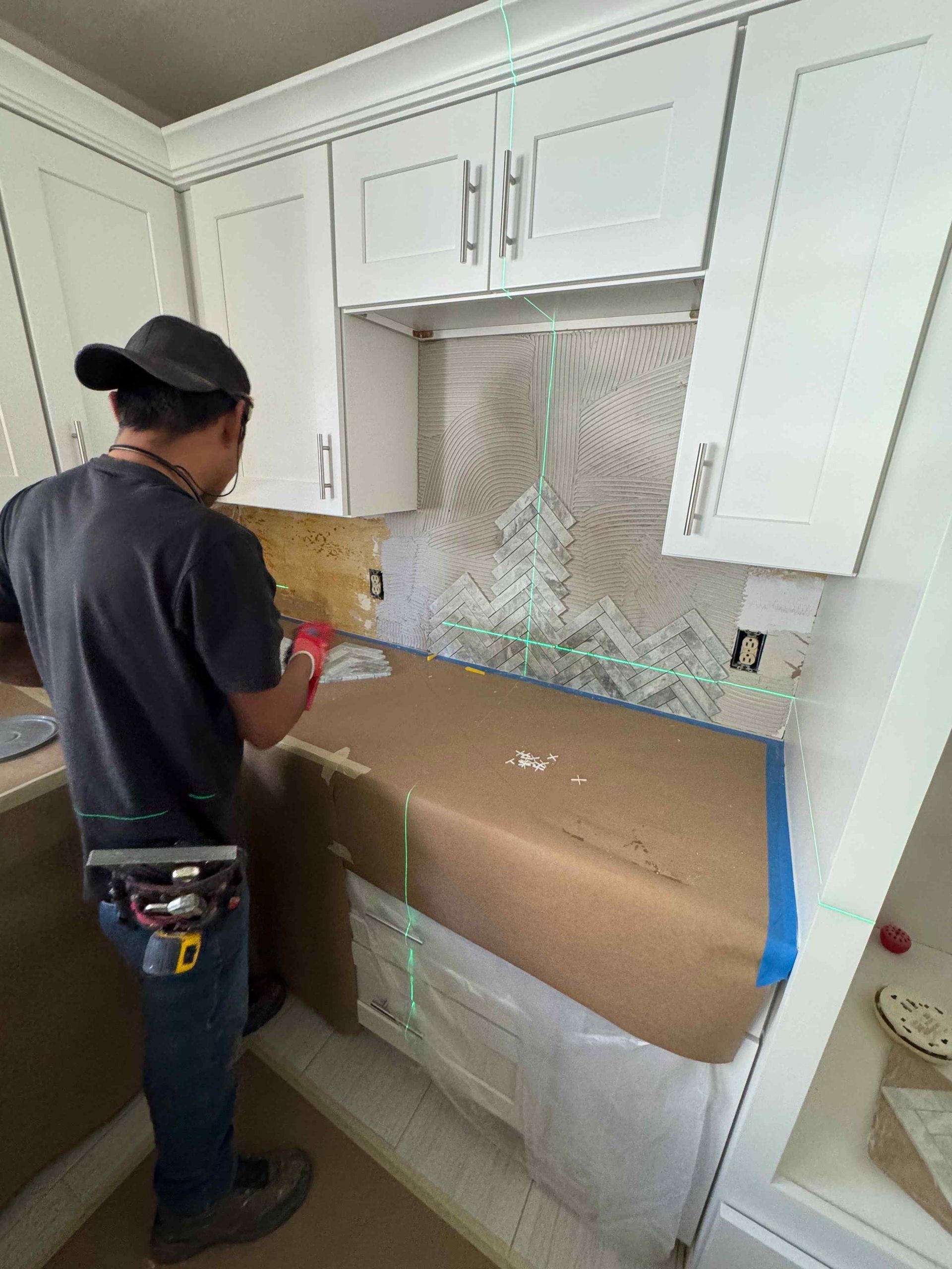 Person installing a white kitchen cabinet with a protected countertop and backsplash area