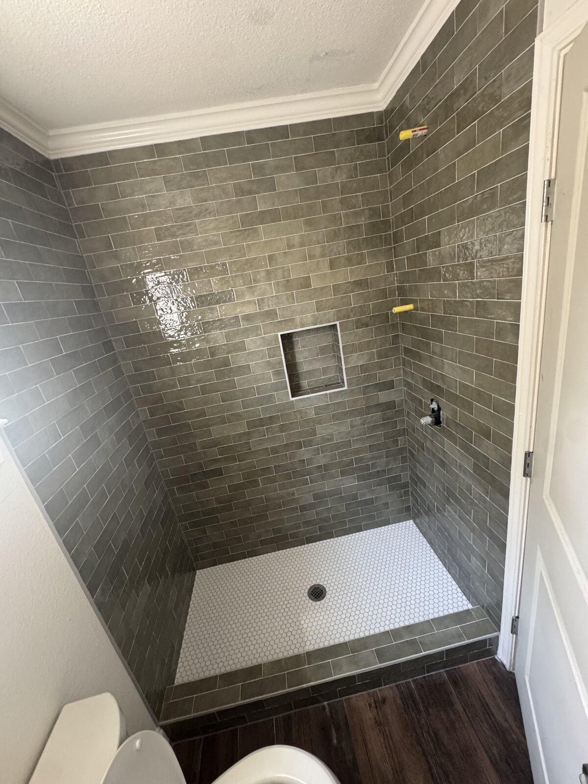 Remodeled walk-in shower with olive glazed tile and white penny-tile pan