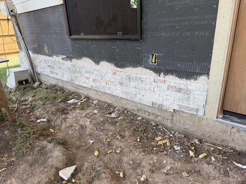 Exterior wall with stone base installed and lath in place before siding