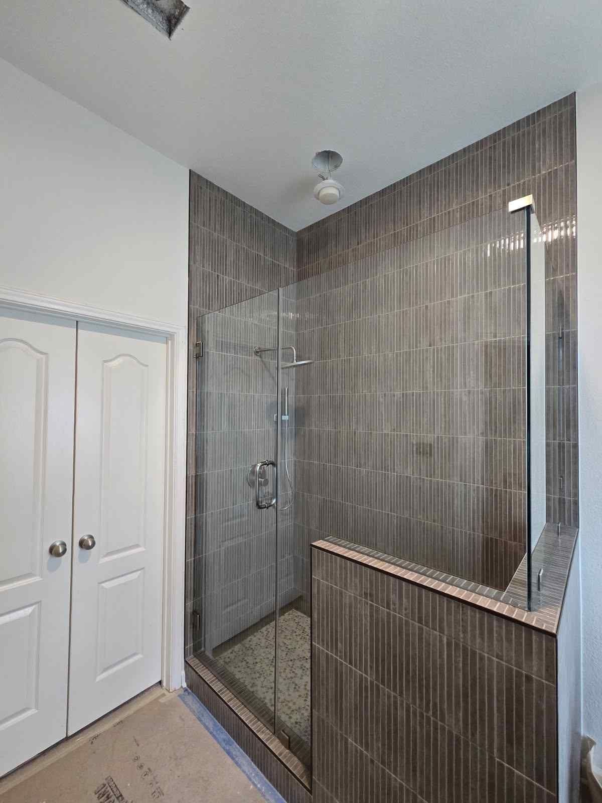 Bathroom with tiled walk-in shower, glass enclosure, and white double-door closet.