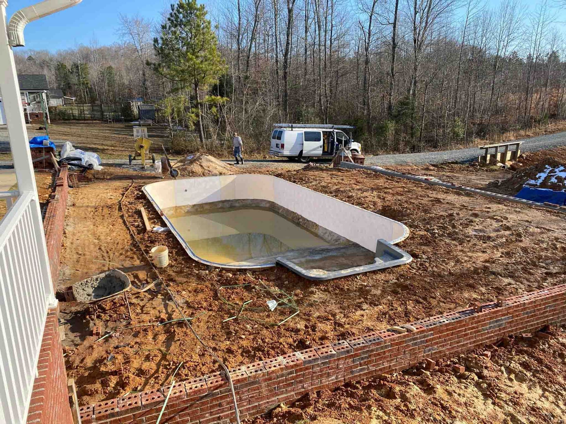 Backyard with an in-ground pool under construction, surrounded by dirt and brick retaining walls.