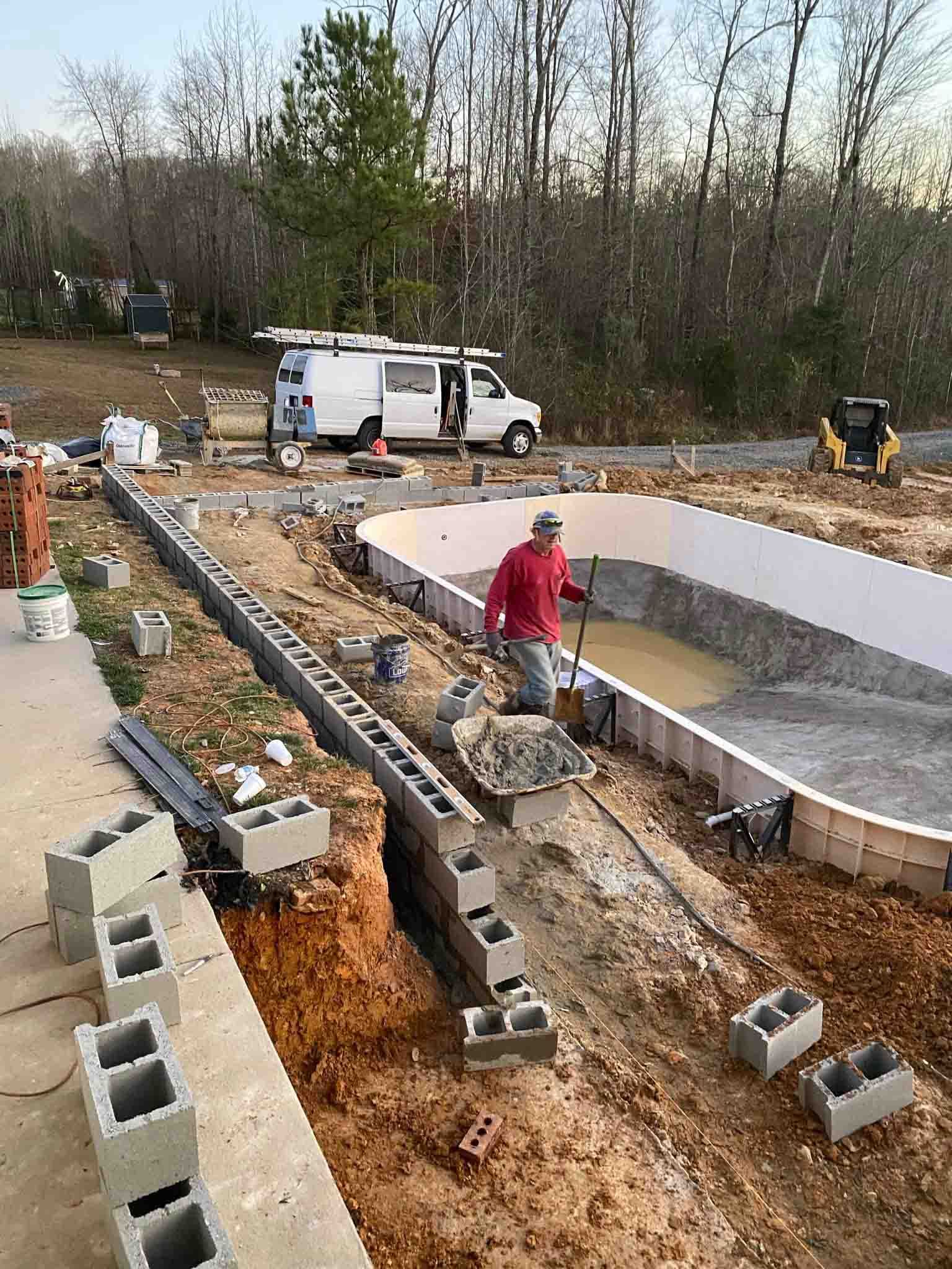 Workers building a curved concrete pool foundation at a construction site with cinder blocks and a white truck nearby