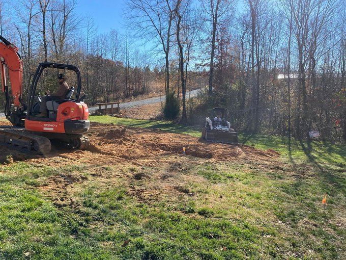 Orange excavator clearing dirt on a wooded hillside under a clear blue sky
