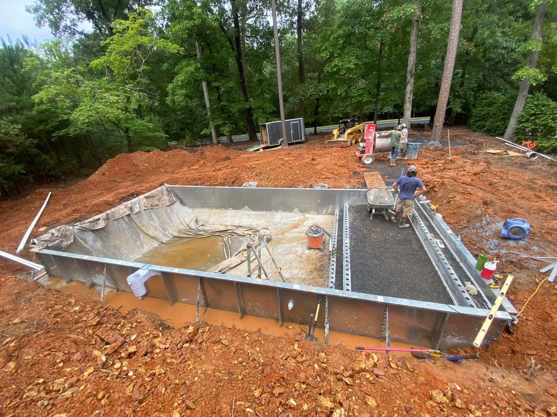 New concrete foundation excavation with rebar forms and workers at a wooded construction site