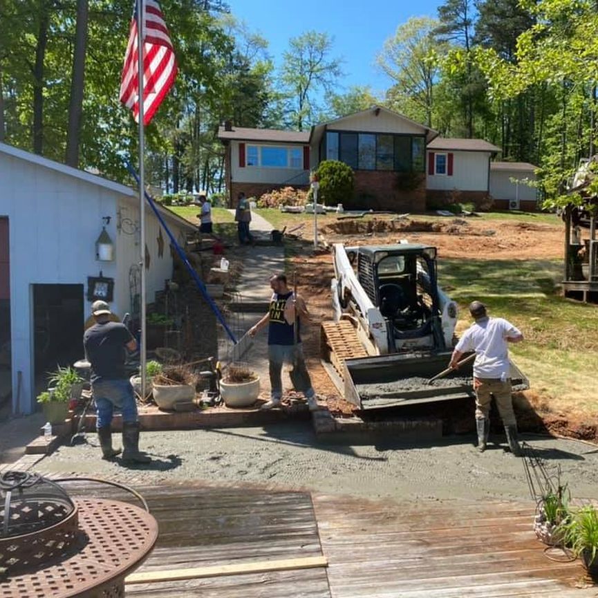 Workers loading debris into a dumpster in a yard beside a house, with an American flag and a pickup truck.
