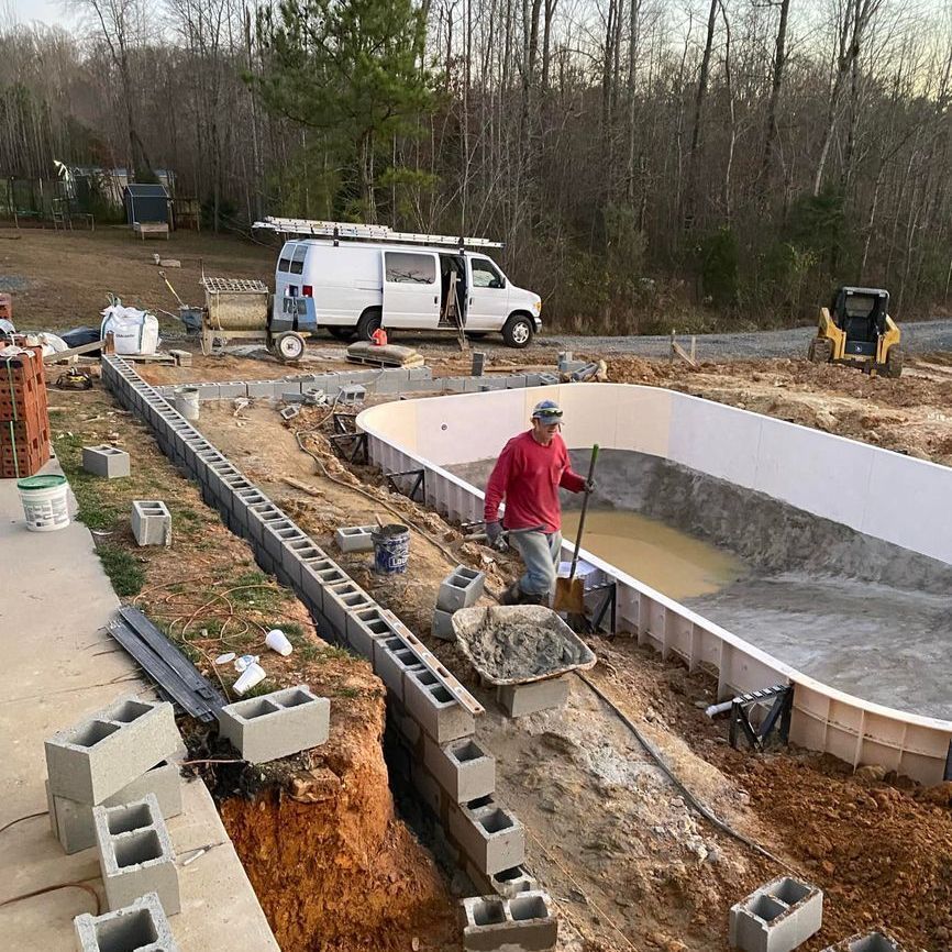 Construction workers forming a curved concrete pool shell at an outdoor worksite.