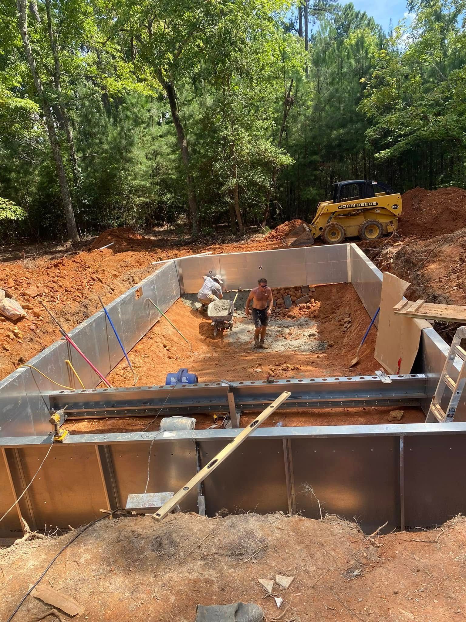 Foundation under construction in a wooded area, with concrete forms and a worker inside the excavation.