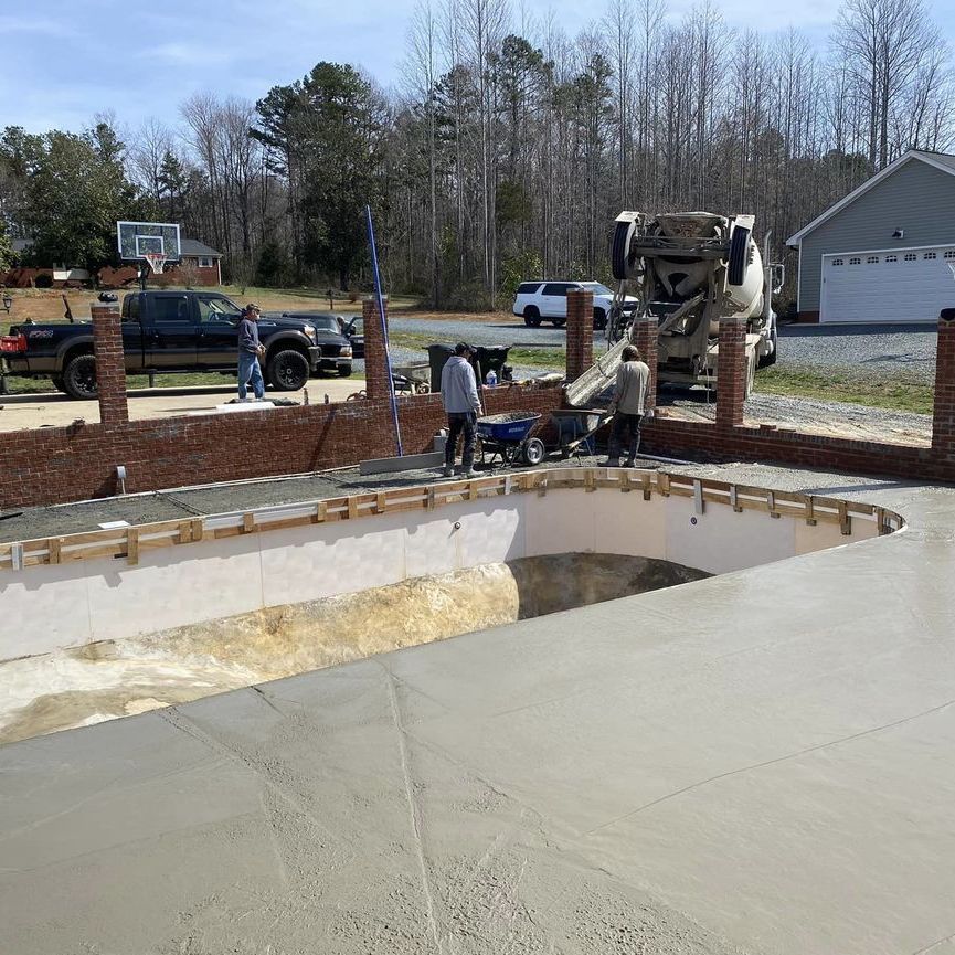 Construction workers building a backyard pool beside a concrete patio and brick retaining wall