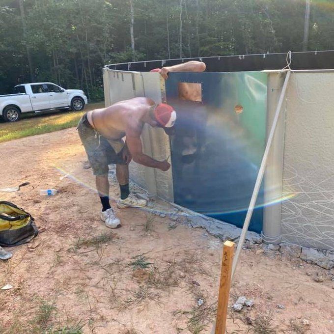Shirtless man bending into a large above-ground tank in a rural yard, with a truck nearby.