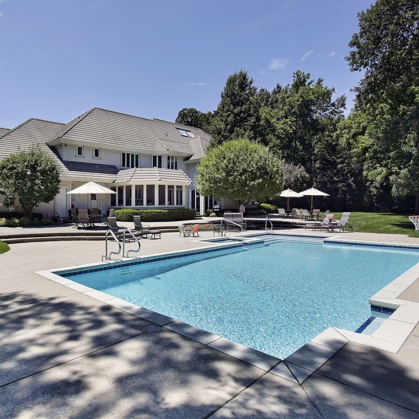 Backyard pool with lounge chairs and white umbrellas beside a large house on a sunny day