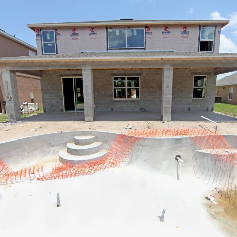 Unfinished two-story house with front porch, exposed cinder blocks, and a partially dug backyard pool area.